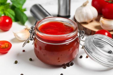 Lezzetli ketçap kavanozu ve beyaz arka planda farklı malzemeler, yakın plan.