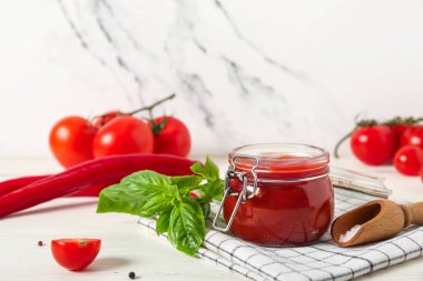 Fesleğen yapraklı ketçap kavanozu ve beyaz ahşap masada kırmızı biber.