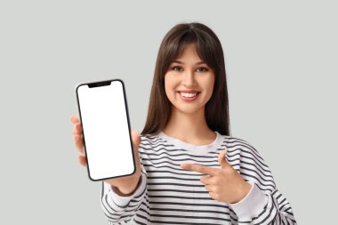 Gülümseyen genç kadın arka plandaki boş cep telefonuna işaret ediyor.