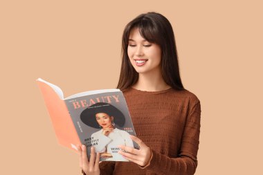 Gülümseyen genç kadın bej arka planda moda dergisi okuyor.