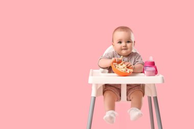Pembe arka planda yüksek sandalyede atıştırmalıkları olan şirin bir bebek.