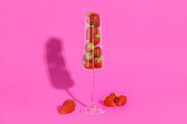 Pembe arka planda taze çilekli şampanya bardağı.