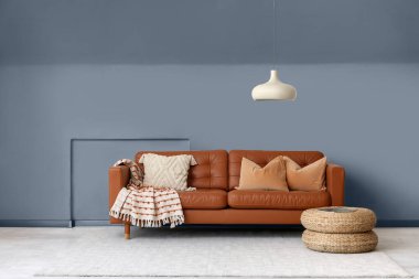 Beyaz duvarın yanında minderleri ve pufları olan kahverengi deri kanepe.