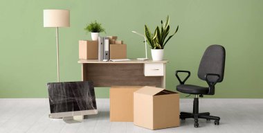 Taşınma gününde iş yerindeki yeşil duvarın yanında karton kutular ve sandalye.