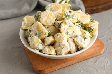 Bir kase lezzetli patates salatası. Gri arka planda yeşiller, yakın plan.