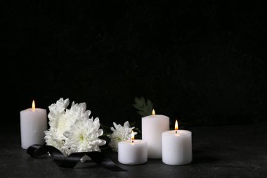 Yanan mumlar, kasımpatı çiçekleri ve arka planda siyah cenaze kurdelesi.