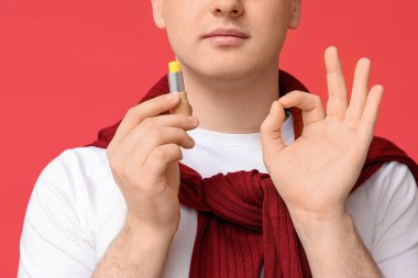 Dudak merhemi olan genç adam kırmızı arka planda iyi bir jest gösteriyor.