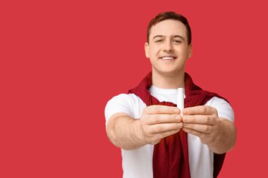 Kırmızı arka planda dudak merhemi olan yakışıklı bir genç.