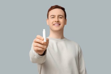 Gri arkaplanda dudak merhemi olan yakışıklı bir genç.