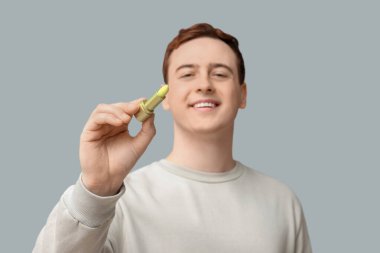 Gri arkaplanda dudak merhemi olan yakışıklı bir genç.