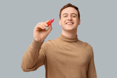 Gri arka planda dudak merhemi olan mutlu genç adam.