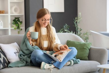 Evdeki kanepede kahve fincanı okuyan genç bir kadın.