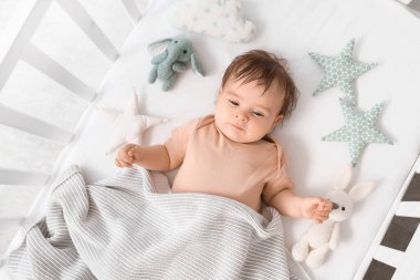 Kareli ve oyuncaklarla beşikte uzanmış şirin bir bebek.