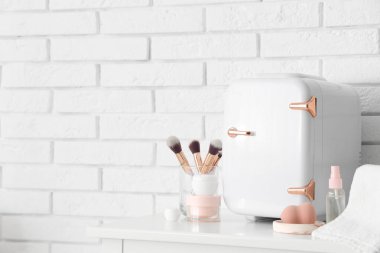 Küçük kozmetik buzdolabı, makyaj fırçaları ve sünger odadaki beyaz tuğla duvarın yanındaki masada. Yakın çekim.