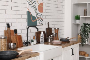 Mutfaktaki beyaz tuğla duvarın yanında farklı mutfak aletleri ve lavabo.