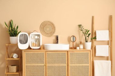 Lavabo, küçük buzdolabı ve kozmetik ürünleri banyodaki bej duvarın yanındaki çekmecelerde.