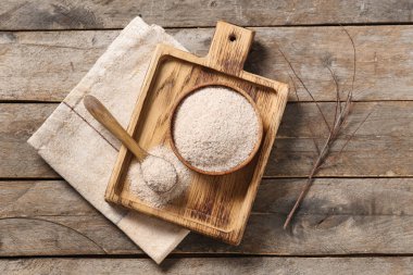 Tahta arka planda psyllium kabuğu tozu olan kase ve kaşık.