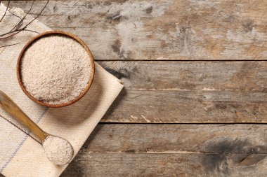 Tahta zemin üzerinde psyllium kabuk pudrası olan kase ve kaşık.