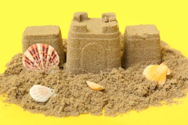 Sarı arka planda deniz kabukları ve mercanlarla güzel bir kumdan kale.