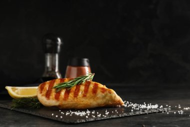 Lezzetli ızgara tavuk göğsü, limon dilimi ve siyah grunge masasında biberiye.