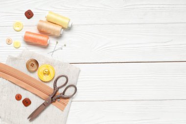 Beyaz ahşap arka planda iplik makaralı farklı renkli düğmeler, kumaş örnekleri ve makaslar
