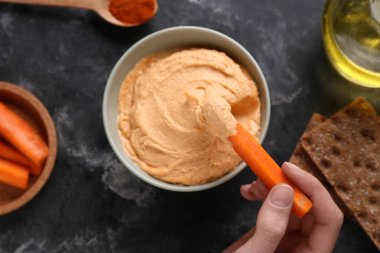 Lezzetli humus yiyen bir kadın ve siyah grunge arka planında taze havuç çubukları.