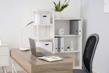 Workplace with laptop and lamp in light office