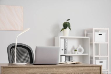 Workplace with laptop and lamp in light office