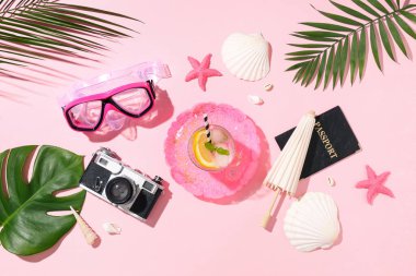 Yaz kompozisyonu plaj aksesuarları, bir bardak kokteyl ve pembe arka planda tropikal yapraklar.