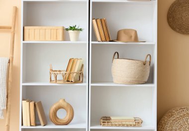 Odada bej duvarın yanında sepet ve şapka olan bir kitaplık.