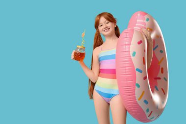 Küçük kızıl saçlı kız şişirilebilir yüzük ve mavi arka planda kokteyl.