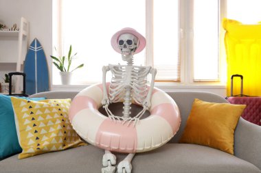 Yazlık şapkalı ve yüzme yüzüklü insan iskeleti oturma odasında kanepede.