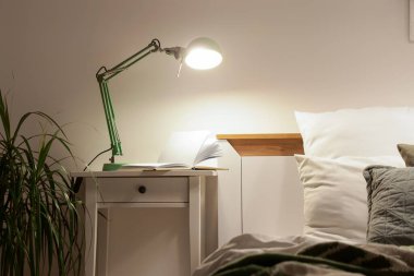 Gece yatak odasındaki masada kitap olan parlak lamba.