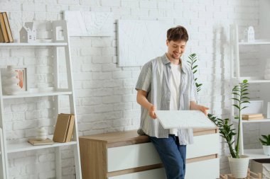 Evindeki beyaz tuğlalı duvarda resimleri olan genç bir adam.