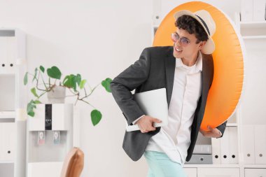 Dizüstü bilgisayarı ve yüzme yüzüğüyle genç işadamı yaz tatilini ofisinde bekliyor.