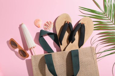 Şık hasır ayakkabı terlikleri, çanta, bir şişe güneş kremi ve pembe arka planda yeşil yaprak, yakın plan.