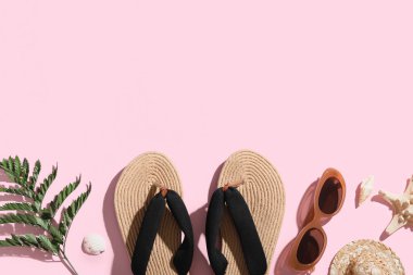 Pembe arka planda şık hasır ayakkabı, güneş gözlüğü ve yeşil yapraklı kompozisyon, yakın plan.