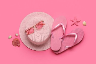 Pembe arka planda şık terlikleri, güneş gözlükleri ve şapkası olan kompozisyon