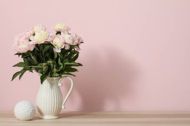 Odadaki pembe duvarın yanındaki masada güzel şakayık çiçekleri olan vazo, yakın plan.