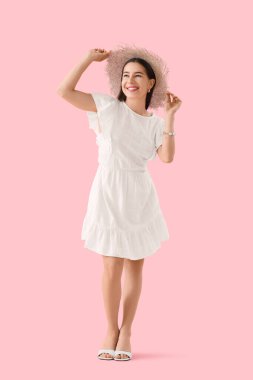Pembe arka planda yaz şapkalı şık genç kadın.