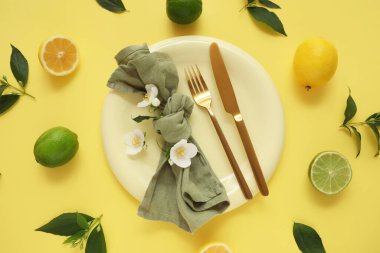 Altın çatal bıçak seti, turunçgiller ve sarı arka planda çiçekler, yakın plan.