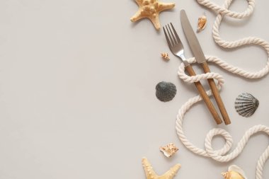 Çatal bıçak, ip ve bej arka planda deniz kabukları olan güzel bir masa.