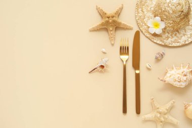 Altın çatal bıçak, şapka, deniz yıldızı ve bej arka planda deniz kabukları ile güzel bir kompozisyon.