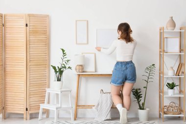 Odadaki ışık duvarına boş bir çerçeve asan genç bir kadın.