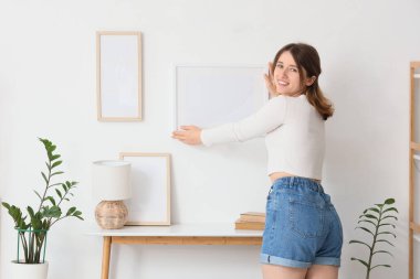 Odadaki ışık duvarında boş bir çerçeve asılı genç bir kadın.