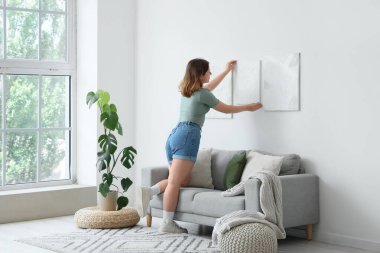 Genç bir kadın oturma odasındaki ışık duvarına resim asıyor.