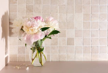 Pembe fayans duvarının yanındaki masada güzel şakayık çiçekleri olan vazo.