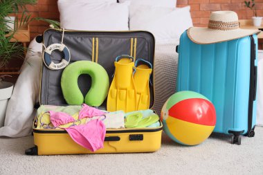 Yatak odasında plaj aksesuarları olan bavullar.