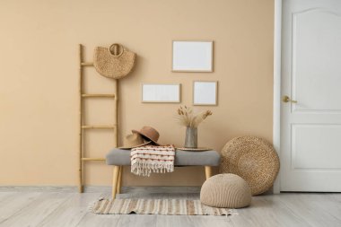 Koridorun iç tarafındaki bej duvarın yanında gri bank, puf ve merdiven var.