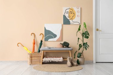 Gri bank, resimler, hasır kutu ve koridorun iç tarafındaki bej duvarın yanındaki ev bitkisi.